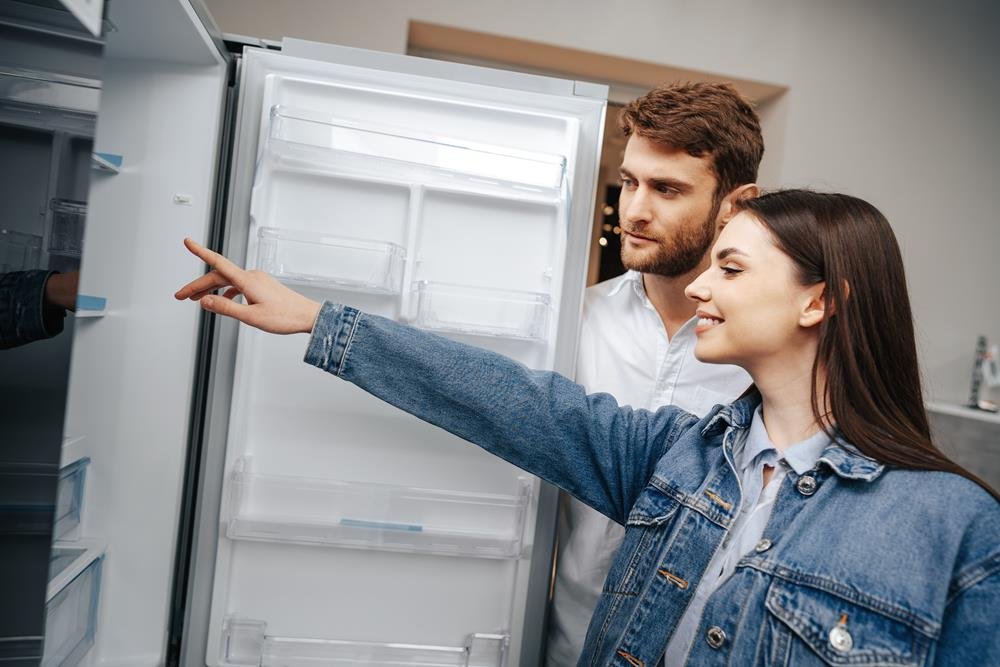 Young couple selecting new refrigerator in household appliance store, close up